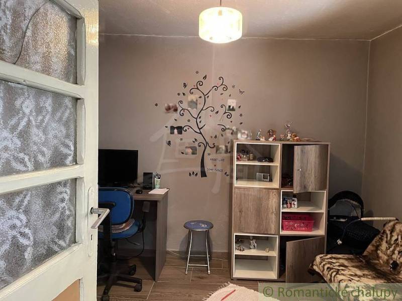 A room in a family house with a desk, a blue chair, a cabinet, and a decorative wall tree.