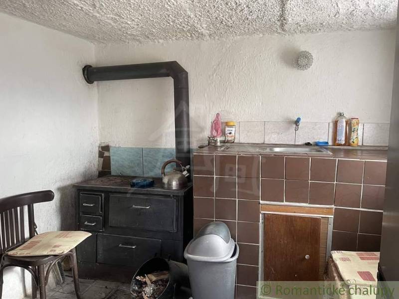 A simple kitchen in a cottage with a stove, sink, and chair in a rustic style.