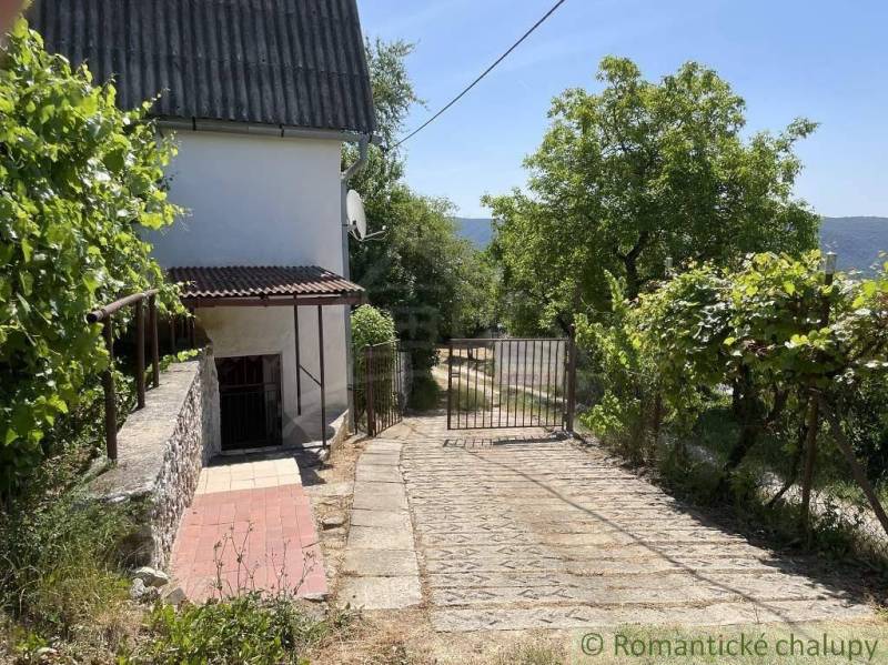 Cottage near Rožňava with an access road, green surroundings, and a gate.