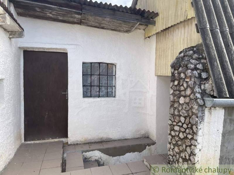 A cottage with white walls, wooden doors, and a stone wall on the terrace.