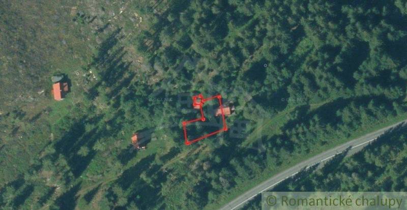 Aerial view of cabins surrounded by forest with highlighted plot for sale.