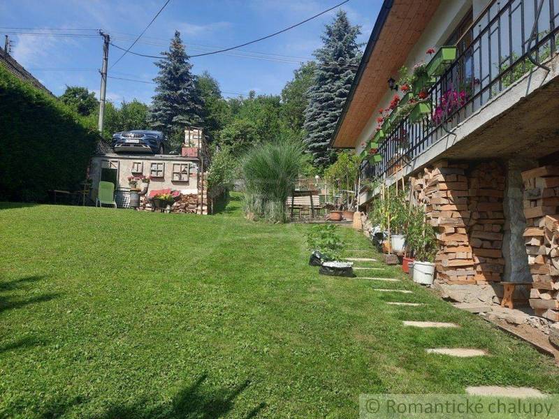 In front of the house, there is a green lawn, flowers on the balcony, and a car by the tree.