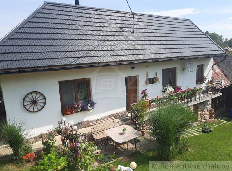 The garden is equipped with a table, windows, and trimmed flowers on the facade of the family house.