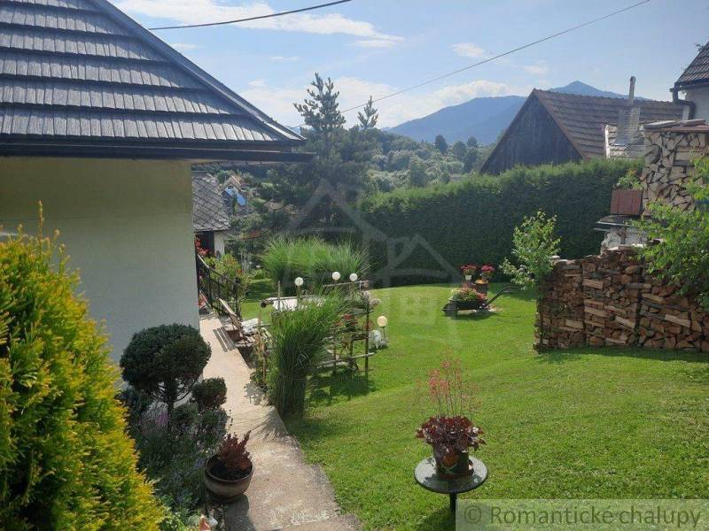 A peaceful garden by the cottage, with flowers around the manicured lawn and a family house.
