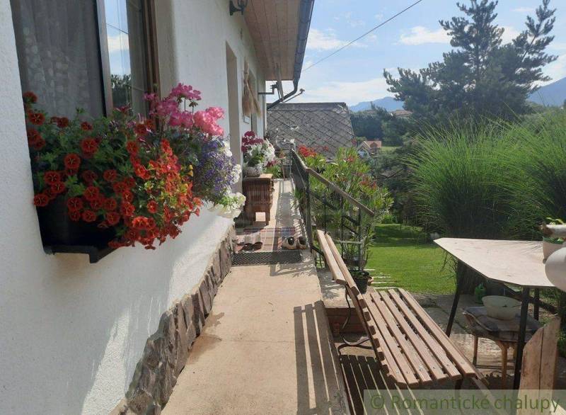 Flower arrangement and a bench on the porch of a family house surrounded by a garden and mountains.