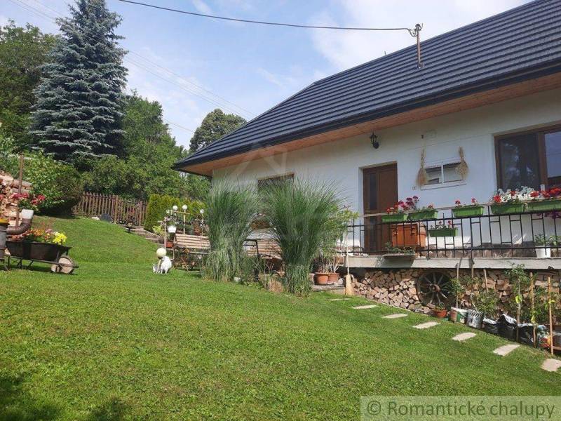 A family house with a wooden roof, flowers on the terrace, and a green garden.