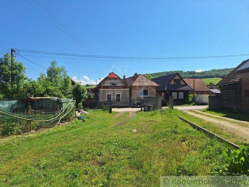 The picture shows rural houses surrounded by a garden and nature in a peaceful setting.