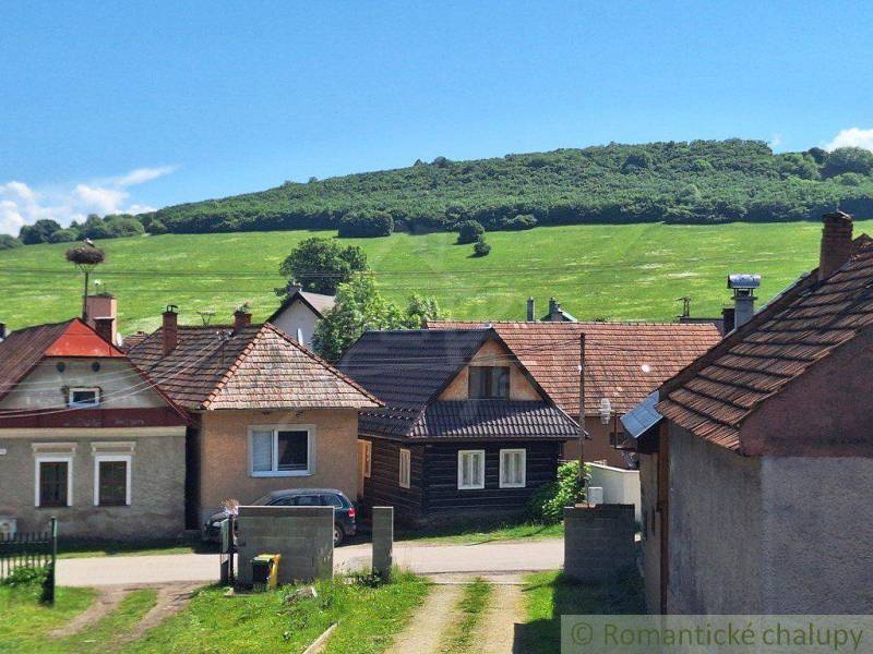 The image shows a row of family houses in the countryside with a green meadow and a hill.