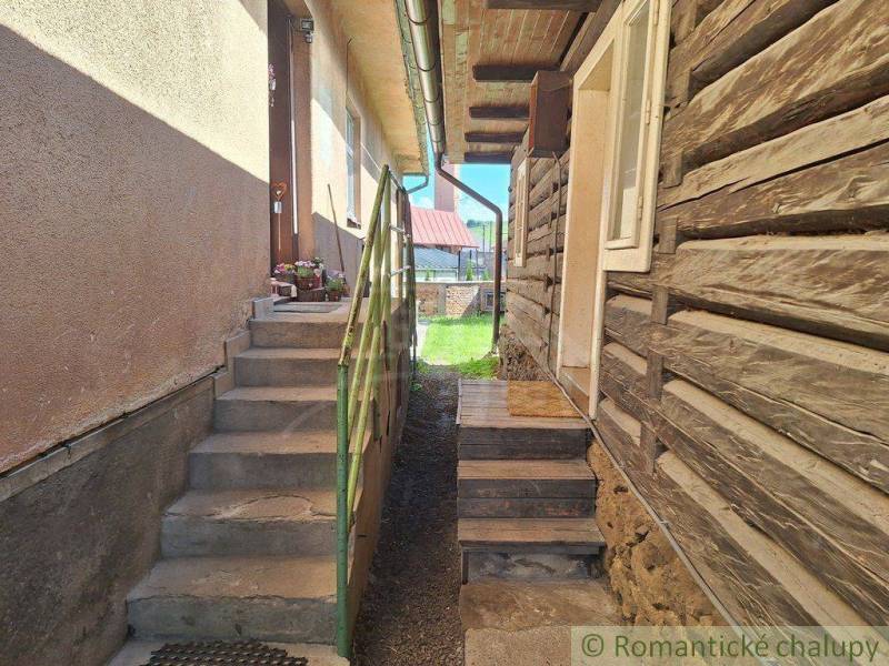 Entrance next to a wooden cottage and family house, stairs, flowers, yard.