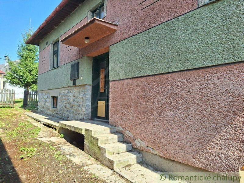 A family house with a colorful facade and a stone foundation, surrounded by greenery and a fence.