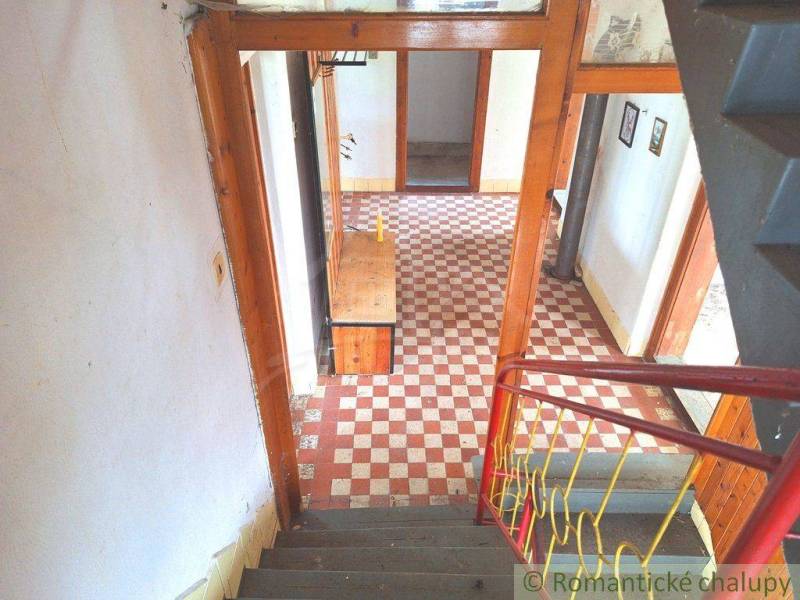 The interior of a family house with a checkered floor, wooden walls, and a staircase with a railing.