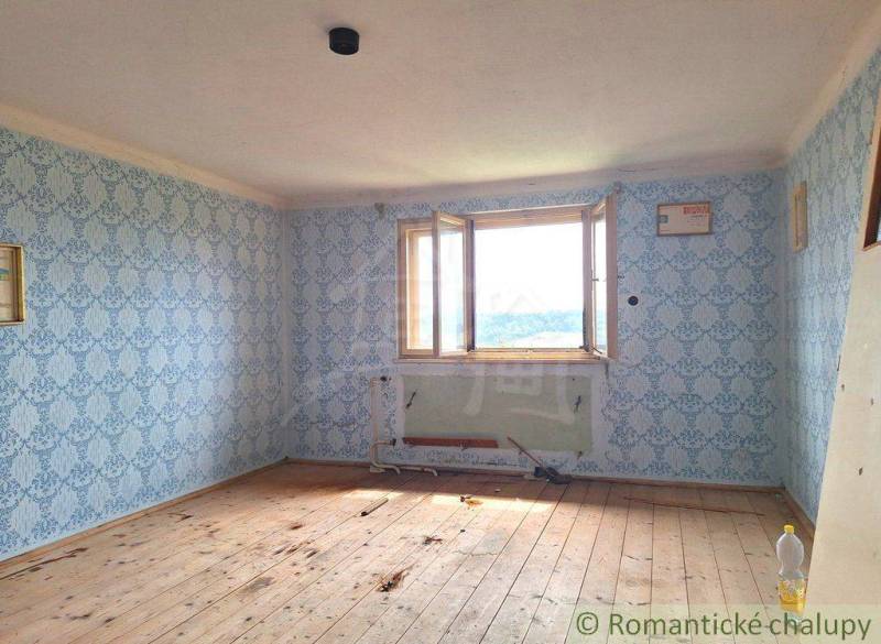 A room with a wooden floor, wallpaper, and an open window in a family house.