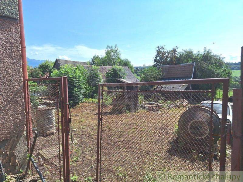 A view through the gate to a yard with vines, a house, and nature in the countryside.