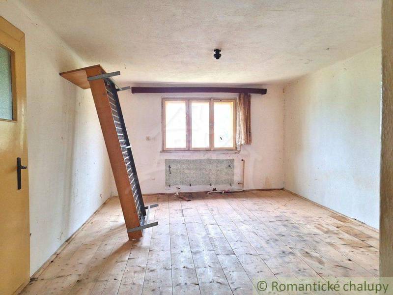 An empty room in a family house with a slanted radiator, wooden floor, and a window.
