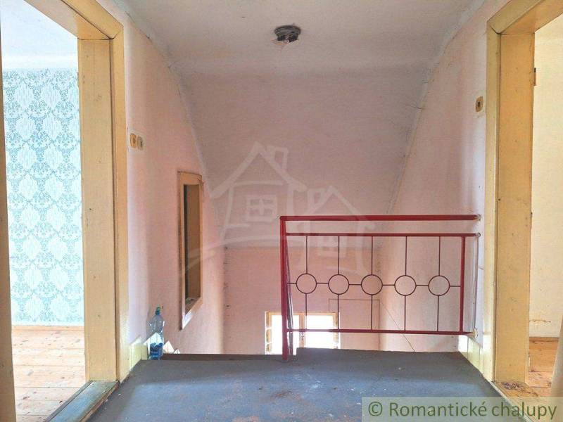 Hallway of a family house with a wallpapered wall, wooden floor, and red staircase railing.