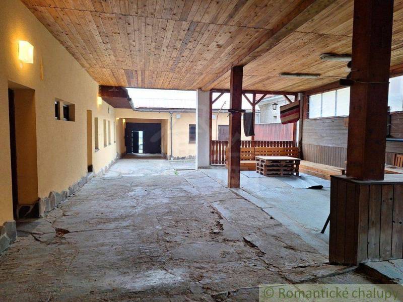 An elongated shelter with a wooden roof, an enclosed area, and a family house with a backyard.
