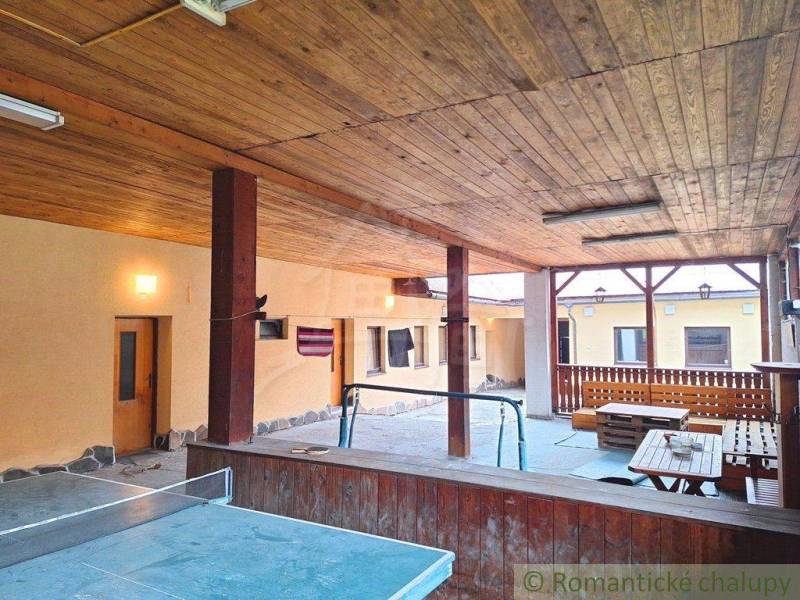 Wooden terrace ceiling with a ping pong table, benches, and a family house in the yard.