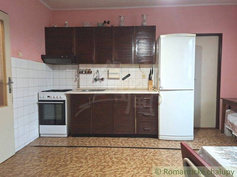 A kitchen with a traditional dark kitchen unit, refrigerator, sink, and stove in a family house.