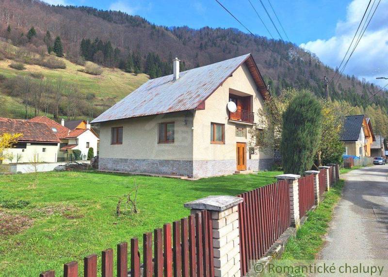 A family house with a wooden fence, a large garden, surrounded by mountains and surroundings.
