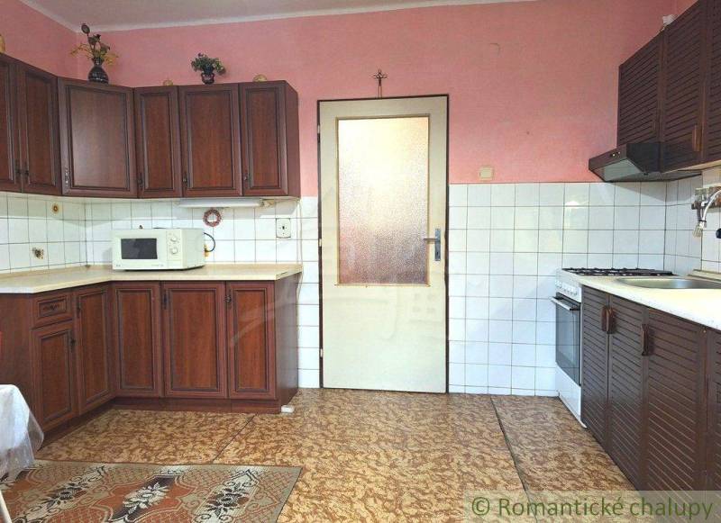 A kitchen in a family house with classic wooden cabinets and white tiles.