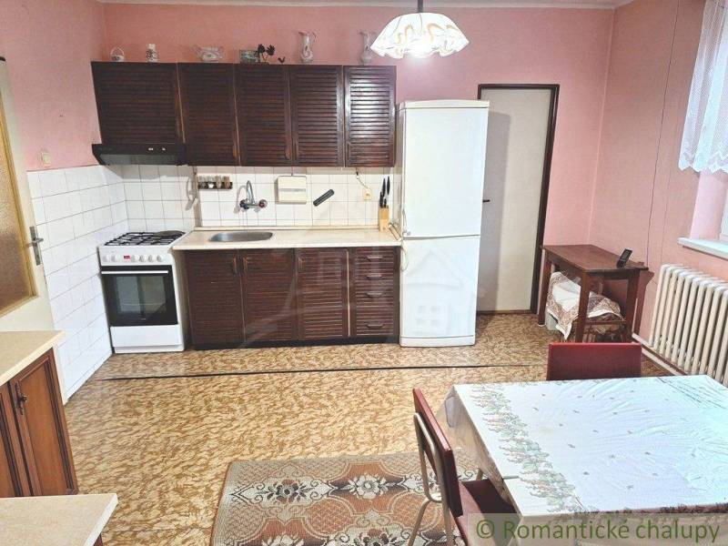 A kitchen with a gas stove, a white refrigerator, Roman blinds, and a family house with pink walls.