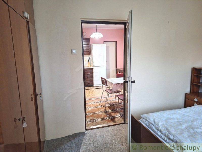 A room with a bed leads to a kitchen with a refrigerator in a family house.