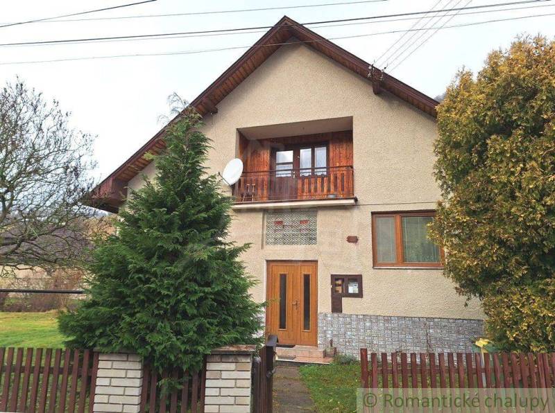 A family house with a wooden balcony, a satellite dish, and a garden behind a wooden fence.