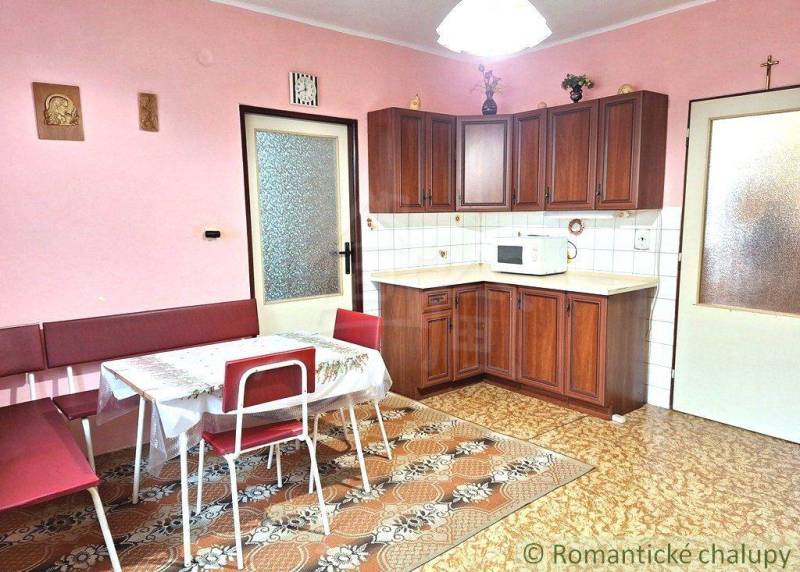 A kitchen in a family house with wooden cabinets, a table, and pink walls.