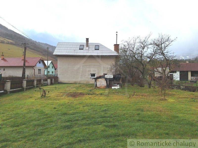 A family house with a metal roof, a garden with a lawn, trees, and a country fence.