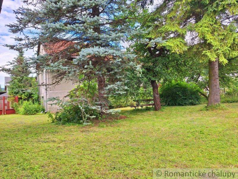 Peaceful residential plots with large trees, a bench, and a house in the background.