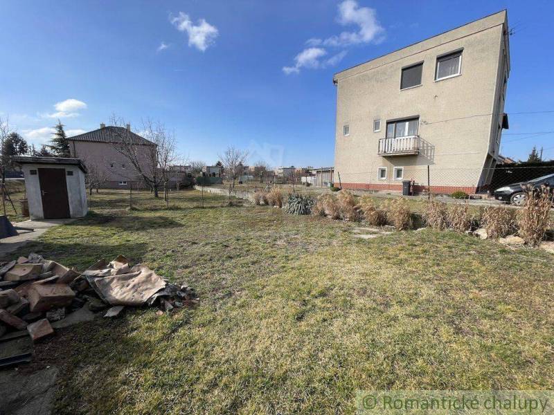A family house with a lawn, a shelter, blue sky, and a garden with plants.