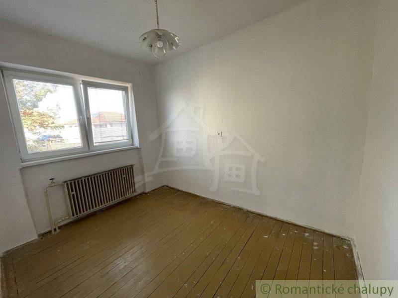 An empty room with wooden flooring, a radiator, and a window, and a family house.