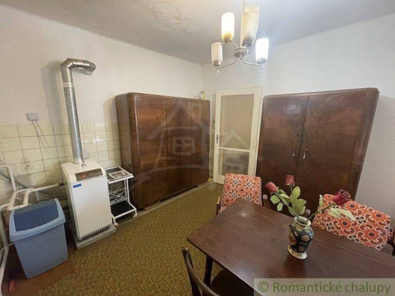 A kitchen with a tiled stove and wooden cabinets, a table with a flower vase complements the space.