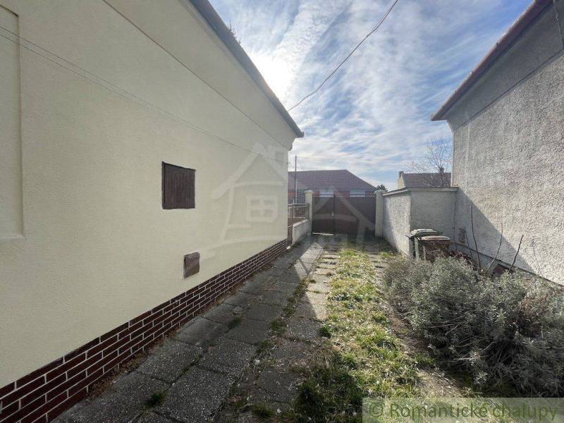 A narrow courtyard of a family house with a concrete path leads to a double-winged gate.