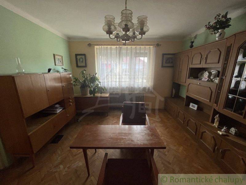 A room in a family house with wooden furniture, houseplants, and curtains on the window.