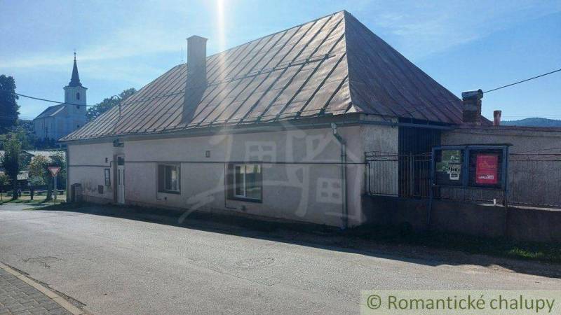 A family house with a gable roof, in front of which is a road and a church in the background.