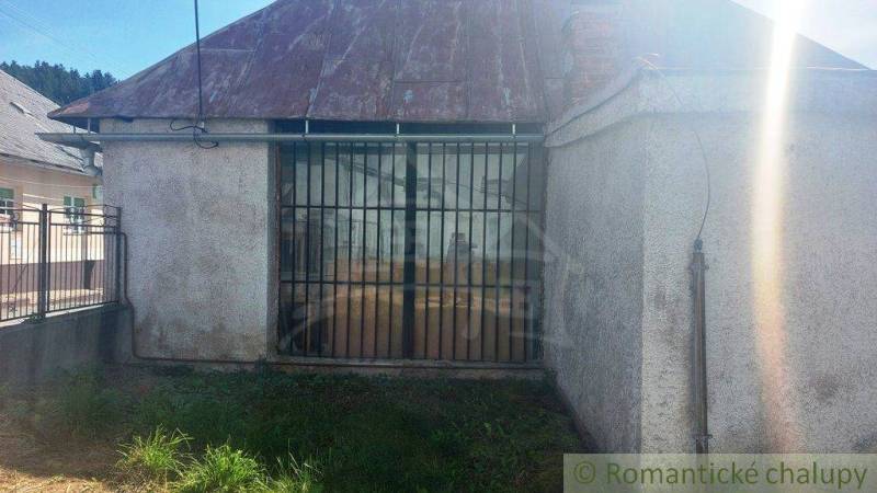 An old building with a neglected roof, metal grille, and fence surrounding a family house.