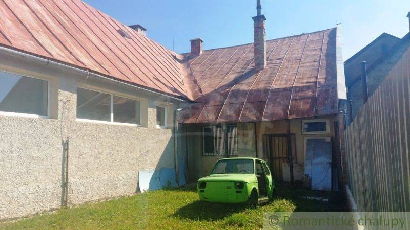 A yard with part of a family house, an old car, and a mowed lawn in the surroundings.