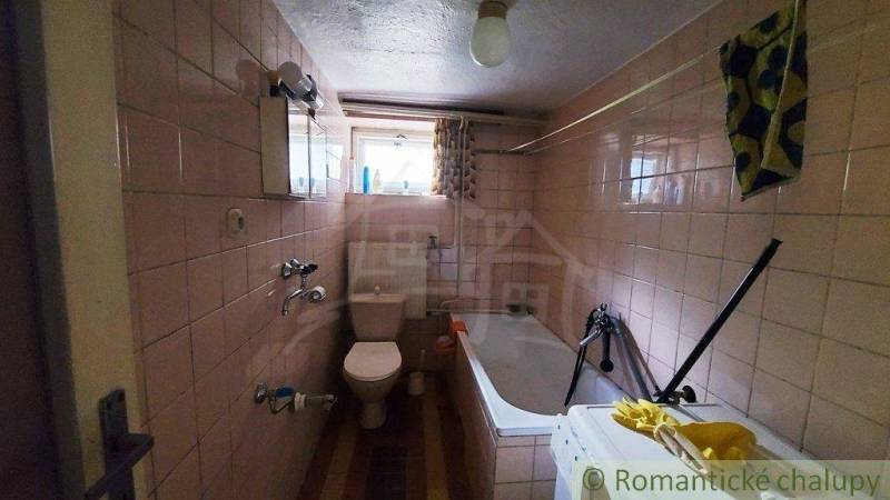 A bathroom in a family house with a bathtub, a sink, white tiles, and a window.