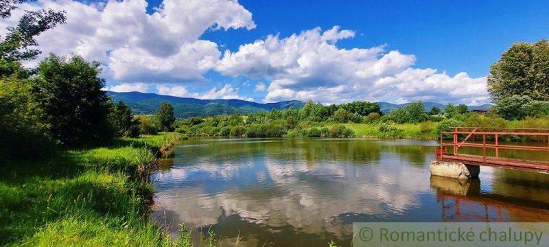 In the picture, there is a tranquil river with a bridge, surrounded by green hills and a blue sky. The area is suitable for plots and living.