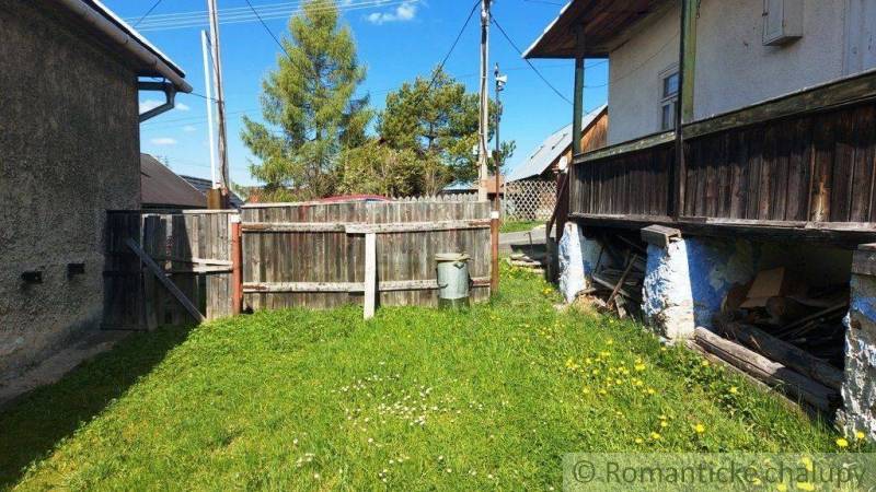 An old yard with grass, a wooden fence, and peculiar properties in the background.