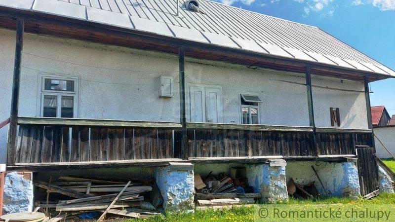 An older cottage with a wooden porch, a metal roof, and a settled white facade.