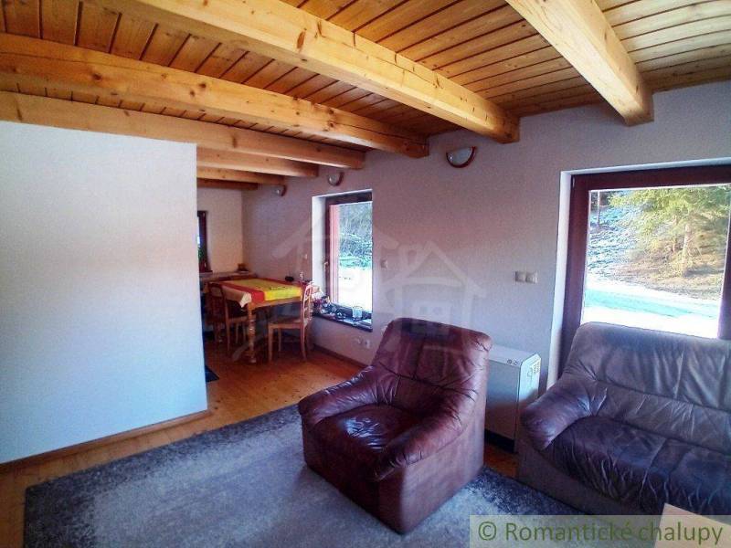 Living room in a cottage with leather armchairs, wooden ceiling, and dining table.