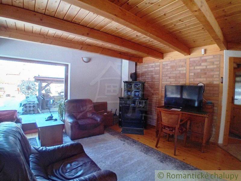A cottage with terrace access, leather armchairs, a television, vintage stove, and wooden ceiling.