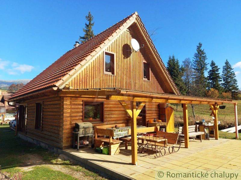 A wooden cabin with a gable roof and a terrace in a natural setting.