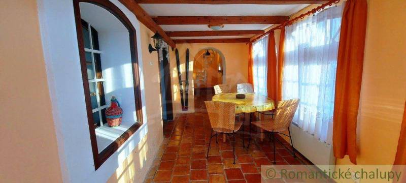 The interior of a cottage with a dining table, brick floors, large windows, curtains, interesting properties.