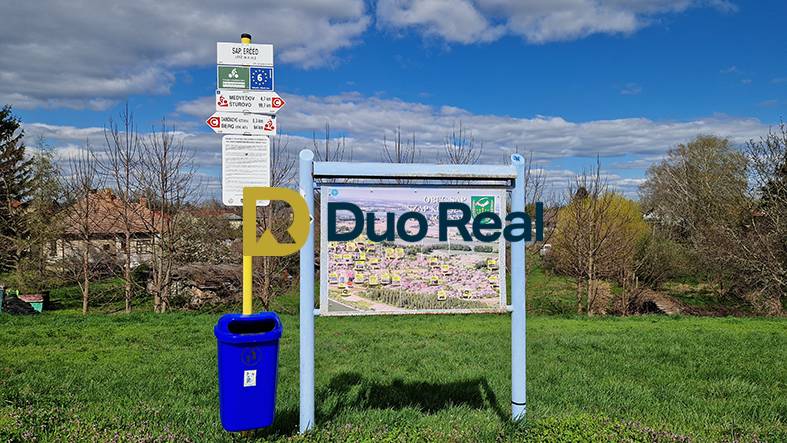 Information board with a map and a bin in the village of Sap near family houses.