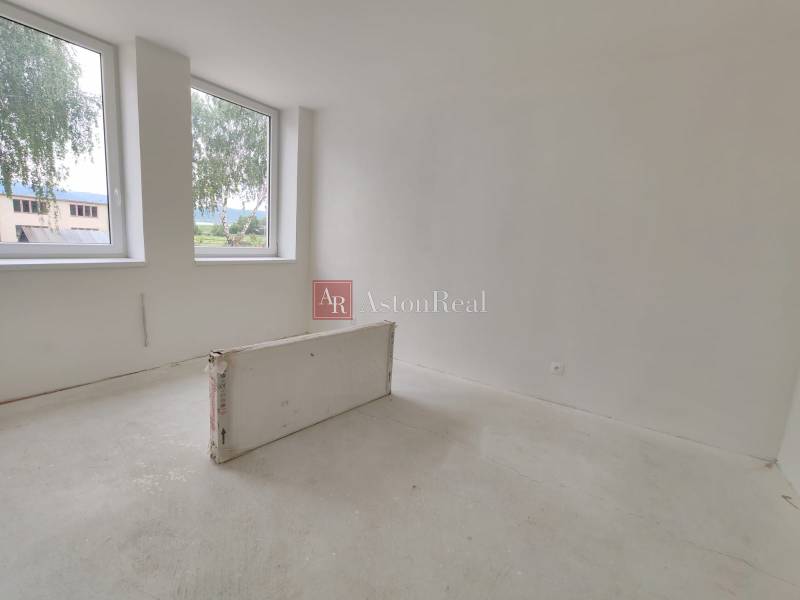 An empty room with two windows in a three-room apartment, white walls, tiles waiting for installation.