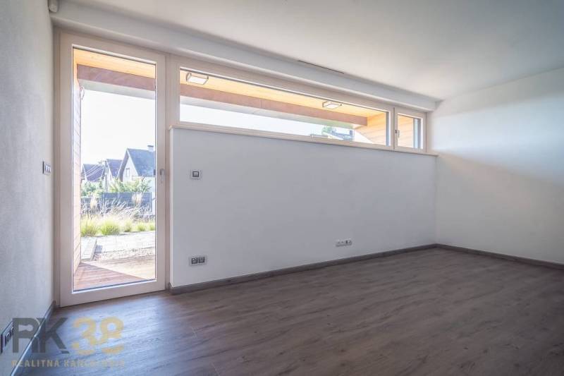 Empty room with a large window, white walls, and wooden floor in a family house.