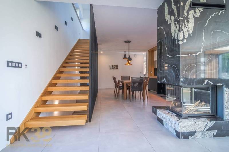 Interior of a family house with wooden stairs, a dining table, and a tiled stove.